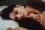 Couple in bed together, the female partner staring straight into the lens of the camera