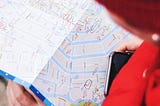 Woman with smartphone glancing at a paper map.