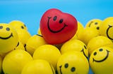 A bunch of yellow balls with smiley faces painted on them with a red heart with a smiley face sitting on top