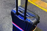 A black suitcase with a rainbow belt at a train station in England