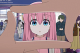 An anime girl with pink hair is framed in a square made by someone’s fingers, looking confused. From the anime Bocchi the Rock!