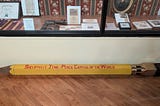 Oversized model of a pencil lying on the floor in front of a museum display case.
