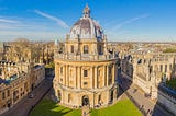 Large stone domed library on campus of Oxford University in England on green grass beneath blue sky