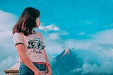 A girl in a pink t-shirt stares at an erupting volcano in the distance
