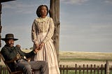 David Oyelowo and Lauren E. Banks as Bass and Jennie Reeves. He sits in a rocking chair while she stands beside him, holding his hand. They are on a porch, and the plains spread behind the fence in the foreground.