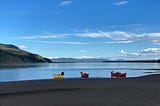 A yellow and two red canoes empty on the banks of the Yukon river.