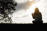 A woman sitting and contemplating in the sunset on a meadow.