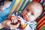 baby holding parent’s hand while looking at camera