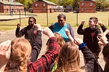 Students standing in circle with adult woman with fists in the air