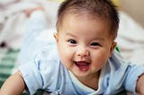 Baby boy lying on stomach with arms propped up, winking.