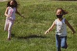 Two young children play outside while wearing COVID-19 face masks.