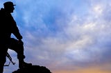 Silhouette of an armed soldier against a blue sky