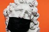 An ancient greek statue with a black medical mask in an orange background.