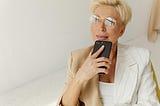 Photo of a Woman with Eyeglasses Holding Her Black Mobile Phone.