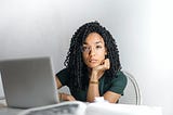 Black woman with green shirt sitting at desk with silver laptop