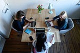 3 women with laptops sitting around a table
