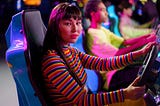 A woman in a colorfully-striped sweater plays a racing game at an arcade