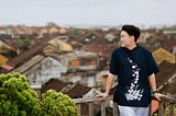 A man leaving on a wooden railing while looking at the view of a town.