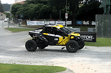 Close up picture of a black and yellow off-road race vehicle speedind across a roundabout.