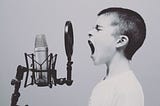 A young white boy shouting into a microphone