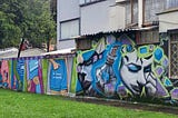 large residential building with a wall on which street artists painted murals. one side is a person with blue eyeshadow and a stoppered bottle of some potion. another side has a four-panel educational mural about reproductive rights.