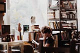 Photo of woman sitting and reading, in a room full of books (Photo by Hatice Hüma Yardım on Unsplash)