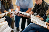 A group of people sitting in a circle reading the Bible.