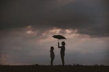 Silhouette of girl holding umbrella over another child