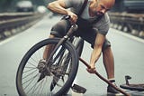 Un hombre en bicicleta introduciendo un palo de madera en la llanta delantera.