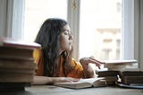 Woman sitting at a desk reading through stacks of books