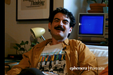 A man in his 20s with a mustache and wavy hair smiling at the camera.