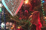 very close-up photo of a christmas tree branch with tiny lights, a red cardinal perched on a branch and a silver metal heart with perforations and a golden light shining on a string of colored beads