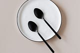 white enamel plate with two black spoons on it with a plain light colored background.