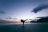 Figure in karate pose on beach at sunset