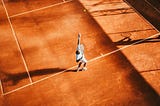 A bird’s eye view of a tennis player preparing to serve a tennis ball.