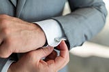 Man in grey suit adjusting cufflinks