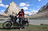 A woman leaning against a bike in front of a giant rock