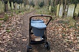 A pram on a path through headstones with trees behind them
