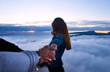 woman peering across an abyss while holding man’s hand.