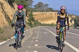 Two female cyclists at least six feet separate ascend the classic Torrey Pines climb in beautiful, sunny San Diego.
