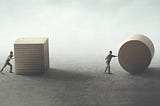 One man pushing a cube, another rolling a cylinder. The man with the cylinder is further ahead.