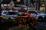A rose bush is wrapped in crime scene tape at the scene of a law enforcement shooting at dusk. Two Solano County Sheriff’s Office vehicles can be seen in the background.