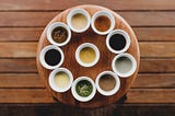 10 different colorful sauces arranged on a wooden serving dish resting on a wooden table.