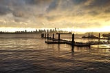 A dock with the silhouette of a city with skyscrapers in the background during a sunset