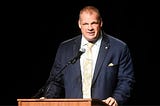 Glenn “Kane” Jacobs behind a podium.