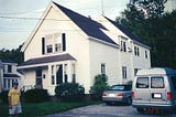 White house with a car and the van in the driveway, with Win looking on, Freeport, Maine, July 22, 2001