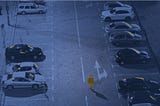 A single highlighted figure walks alone through a field of cars at night