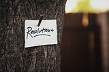 A note that says “resolutions” is nailed to a tree