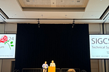 Two projector screens saying SIGCSE 2024 with a podium at the center.
