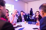 People dressed in business attire, sitting around a table, in a comference room, talking and networking.